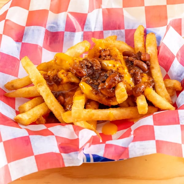 Golden french fries topped with melted cheese and chili, served in a red and white checkered basket.