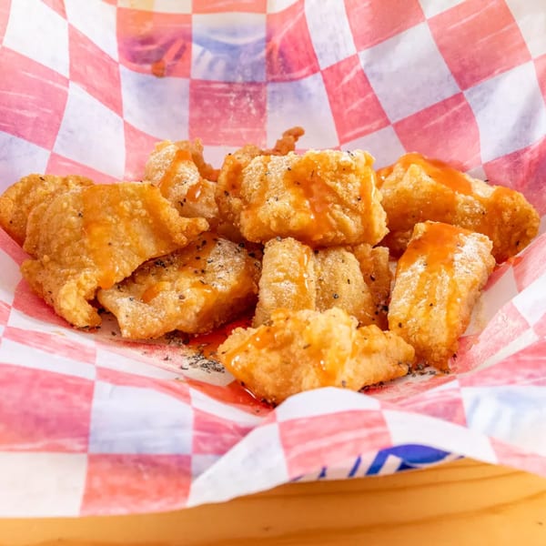 Golden fried chicken nuggets drizzled with orange sauce and sprinkled with seasoning in a red and white checkered basket.