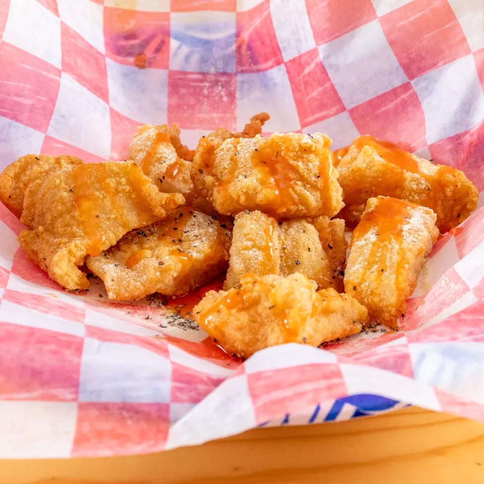 Golden fried chicken nuggets drizzled with orange sauce and sprinkled with seasoning in a red and white checkered basket.