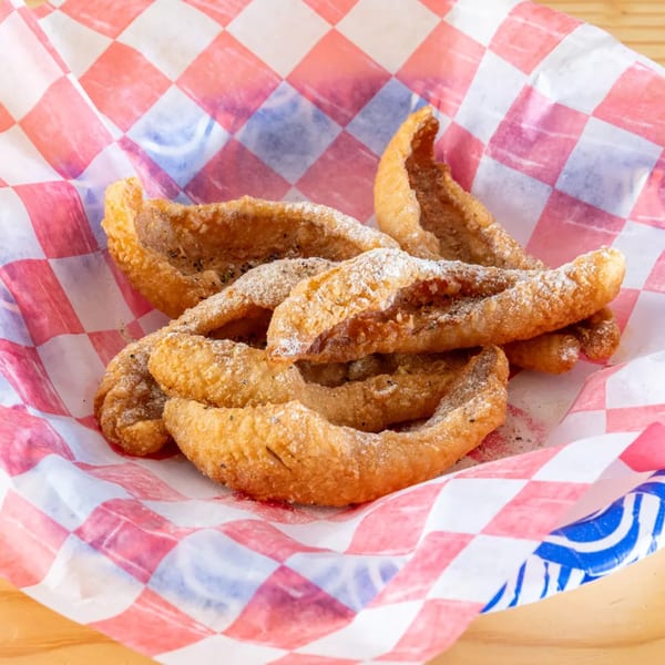Golden fried fish skin cracklings, dusted with seasoning, served in a red and white checkered paper.