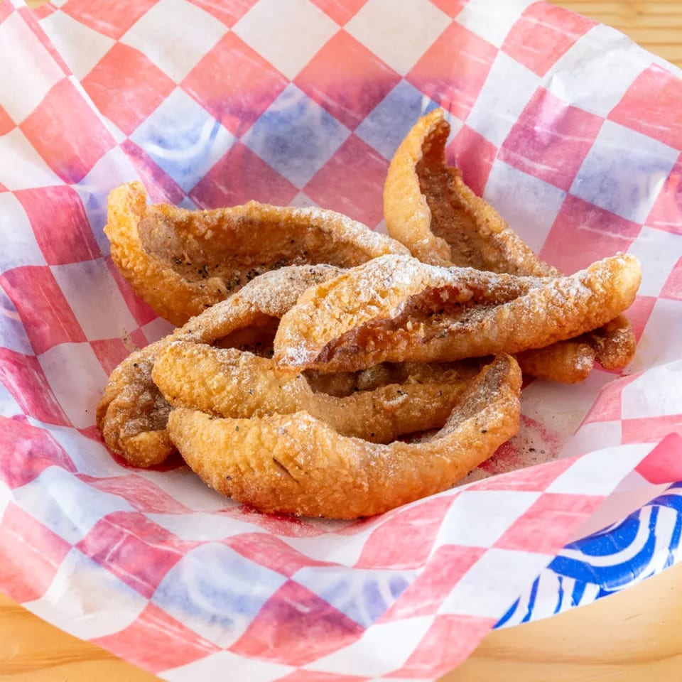 Golden fried fish skin cracklings, dusted with seasoning, served in a red and white checkered paper.
