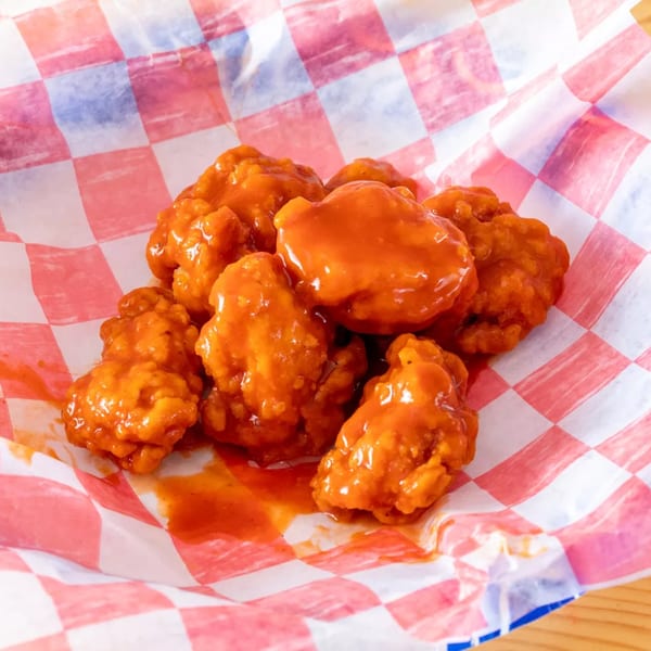 A close-up of boneless buffalo wings, coated in orange sauce, served in a red and white checkered paper.