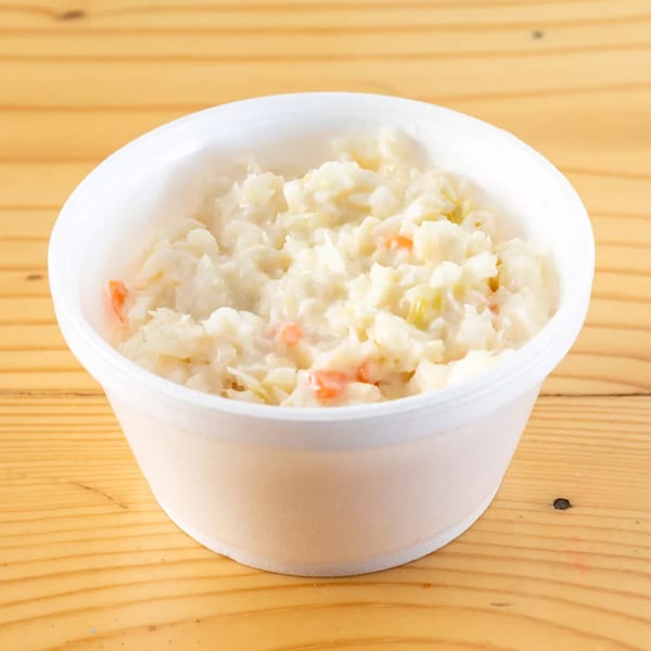 Creamy coleslaw with shredded cabbage and carrots in a white plastic container on a wooden table.