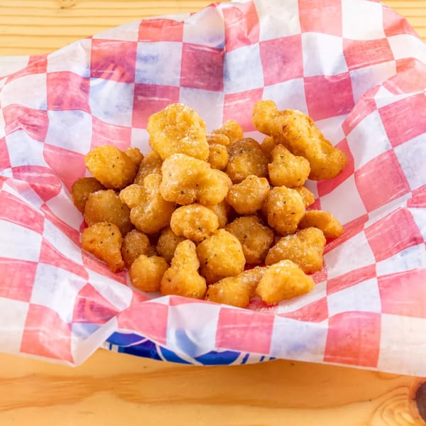 A basket of golden-brown fried cheese curds, seasoned with pepper, in red and white checkered paper.