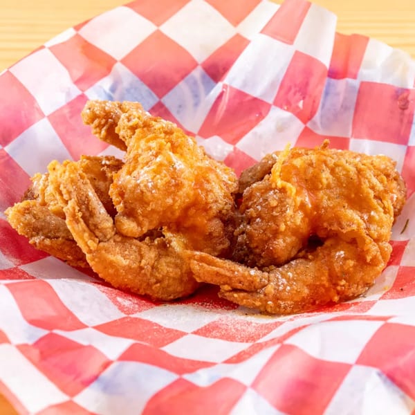 Crispy fried chicken wings, lightly dusted with seasoning, served in a red and white checkered paper basket.