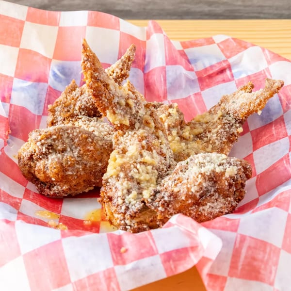 Crispy fried chicken wings coated in Parmesan cheese, served in a red and white checkered paper.