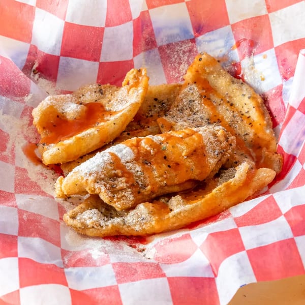 Fried dough pastries drizzled with sauce and powdered sugar in a red and white checkered paper.
