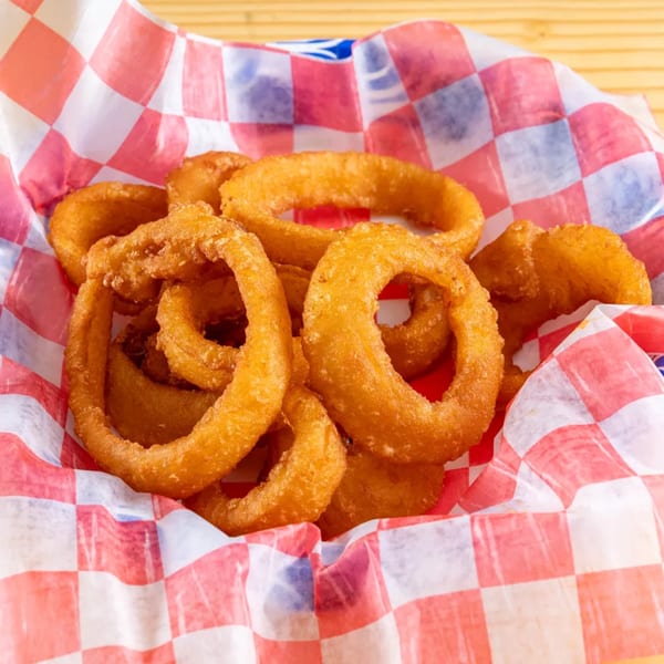 Golden-brown onion rings piled in a red and white checkered paper-lined basket.